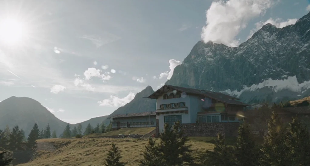 Valkyrie (2008) movie still: establishing — A traditional alpine building is situated at the base of large, jagged, snow-dusted mountains. Sunlight…