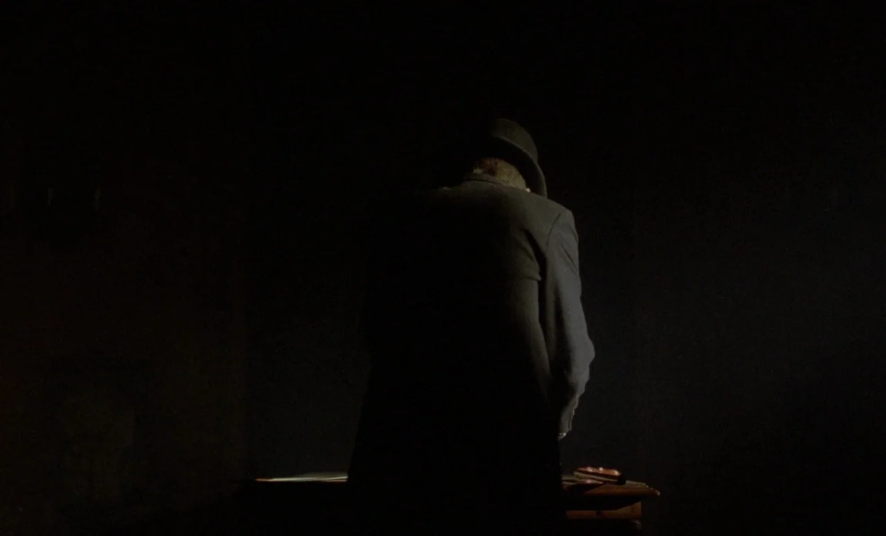 The Strange Case of Dr. Jekyll and Miss Osbourne (1981) movie still: medium — A dark, minimally lit space contains a wooden table with a faint…