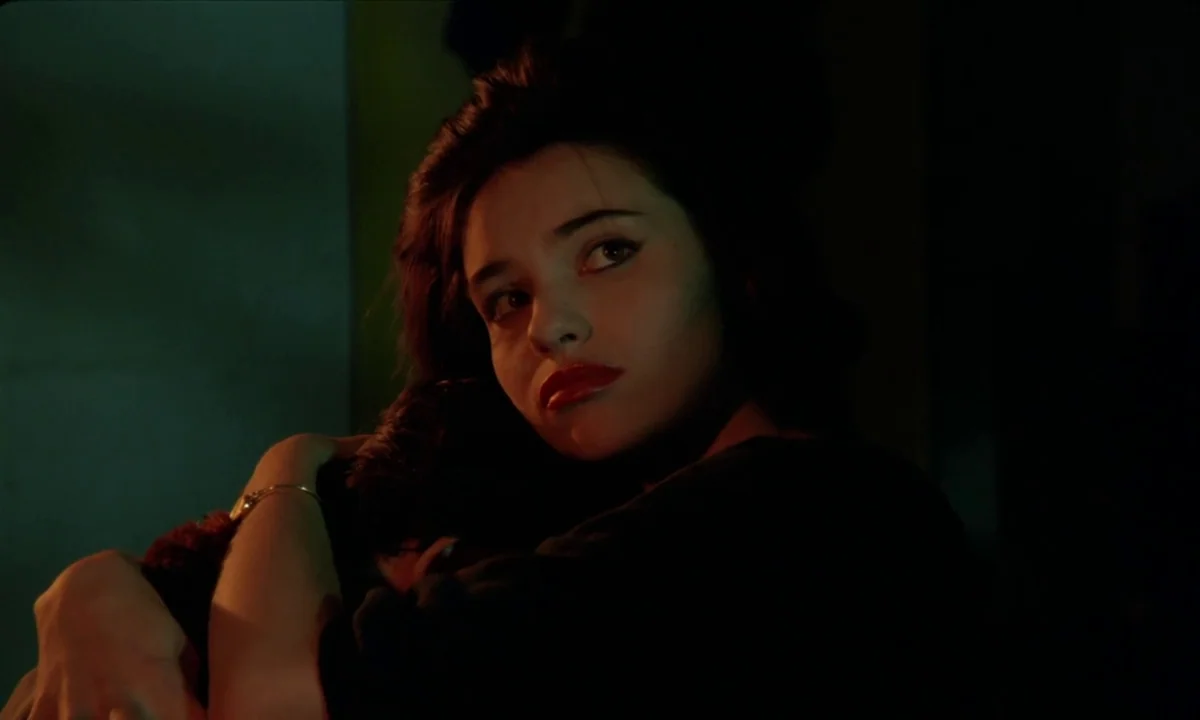 Betty Blue (1986) movie still: closeup — A dimly lit room with high-contrast shadows obscuring the background. A young woman with dark hair holds…