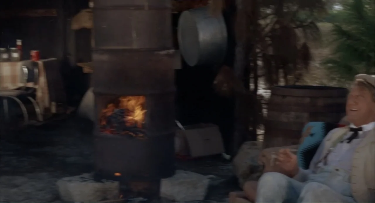 Cottonpickin' Chickenpickers (1967) movie still: medium — An outdoor campsite at night features a makeshift furnace made from a metal drum. A man…