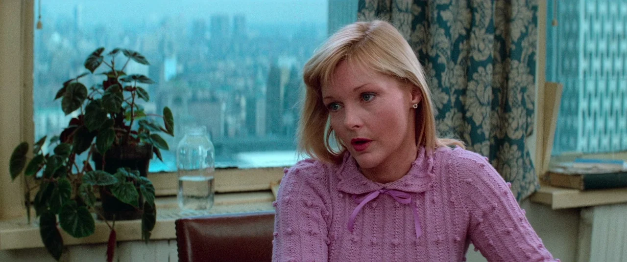 Vigilante (1982) movie still: medium — A bright room features a large window overlooking a hazy, tall city skyline. A woman sits in front of the…