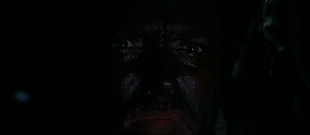 For A Few Dollars More (1965) movie still: closeup — A man's face emerges from deep black shadows in a low light setting. Only his eyes and bridge…