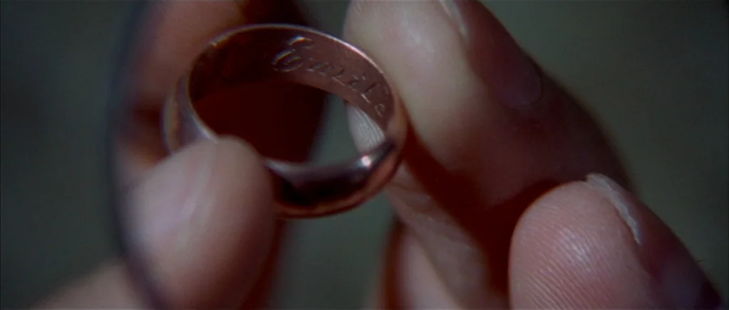 The Private Life of Sherlock Holmes movie still: closeup — A close-up shot focuses on a gold wedding band held between human fingers. The inside of…
