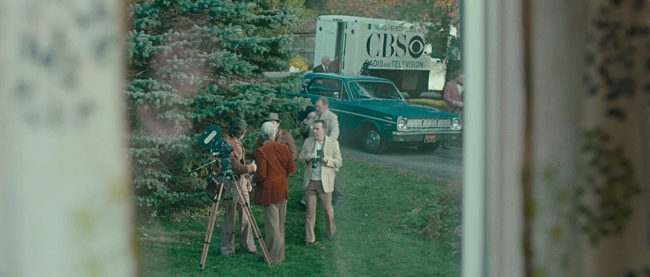 Pawn Sacrifice (2014) movie still: wide — A group of reporters and photographers assemble on a front lawn by a teal car. A white CBS news van is…