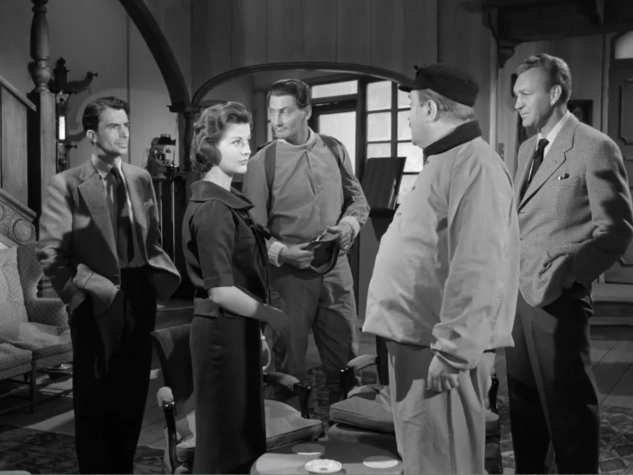 The Crawling Eye (1958) movie still: medium — A spacious room features vintage furniture and wood-paneled walls in a 1950s interior. Five adults…