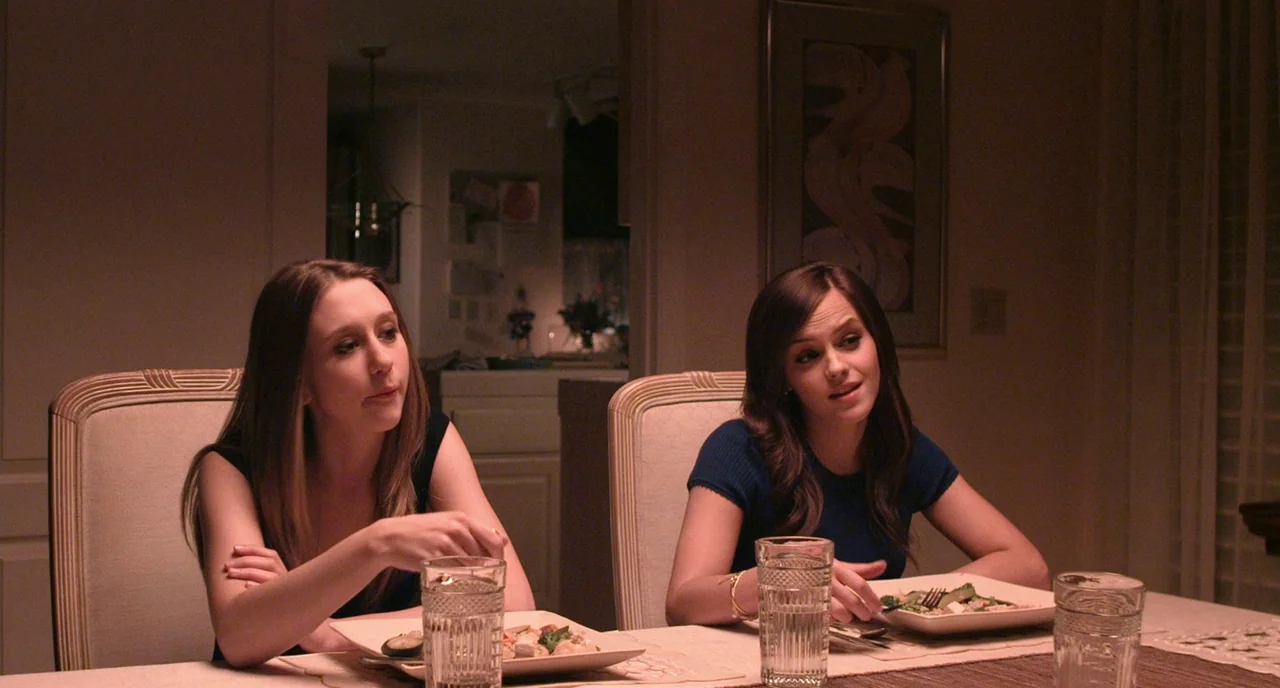The Bling Ring (2013) movie still: medium — Two young women sit at a dining table set for an evening meal. They are engaged in conversation while…