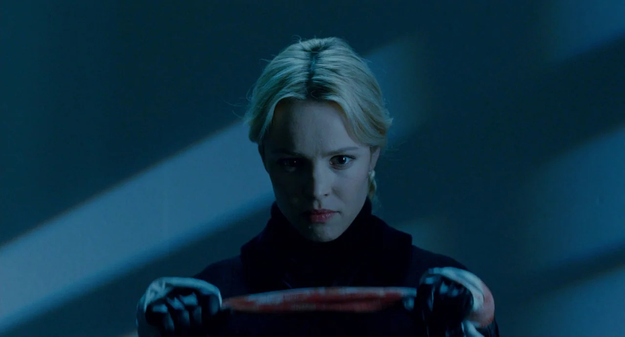 Passion (2012) movie still: closeup — A dimly lit car interior is bathed in cool, nocturnal blue tones. A blonde woman with bloodied gloves grips…