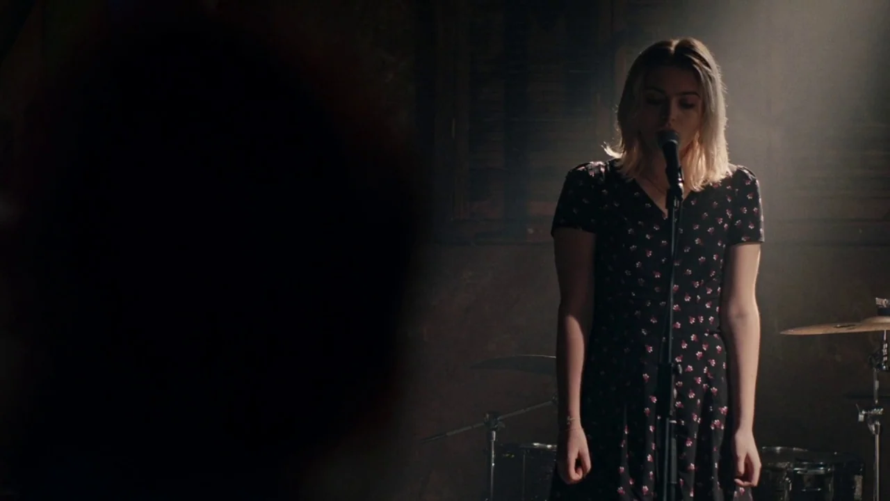 A Date for Mad Mary (2016) movie still: medium — A dark, dimly lit performance space with visible drum hardware in the background. A young woman…
