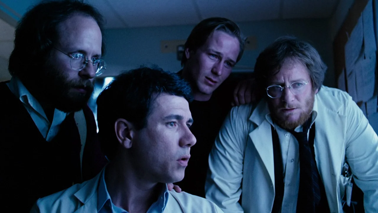 Altered States (1980) movie still: medium — A dimly lit room with blue light illuminating four men clustered together. They watch a monitor intently…