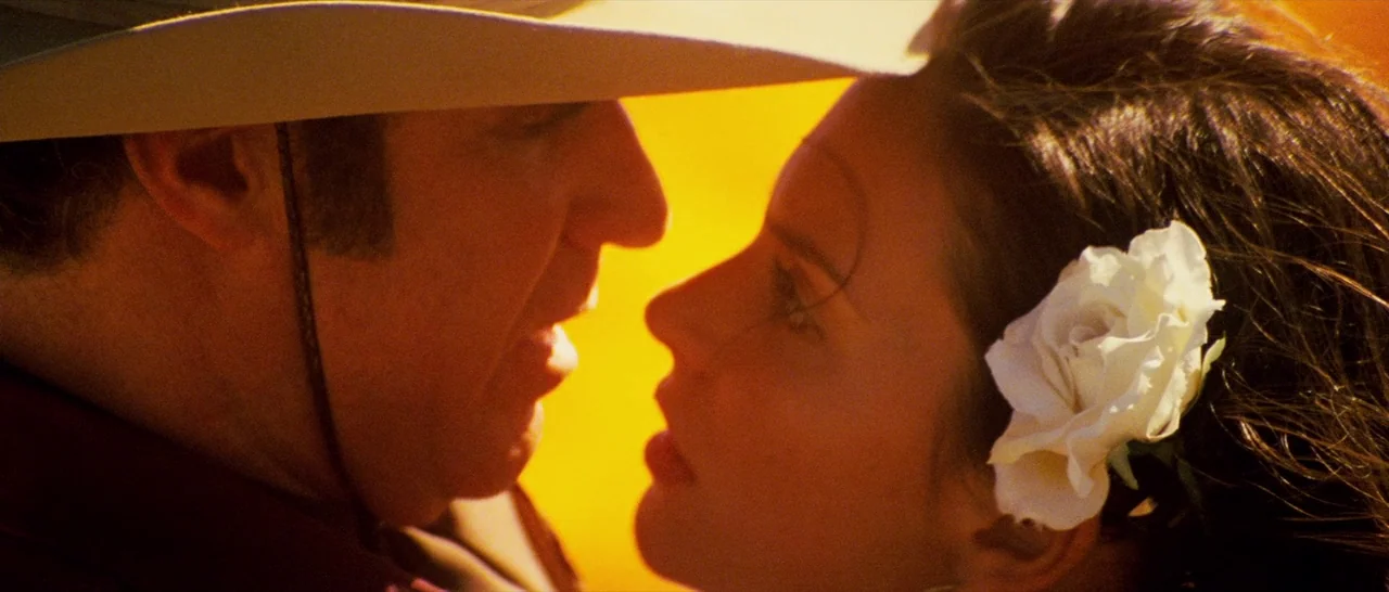 Casa De Mi Padre (2012) movie still: closeup — A man in a cowboy hat and a woman with a flower in her hair. They stand face-to-face in a bright…