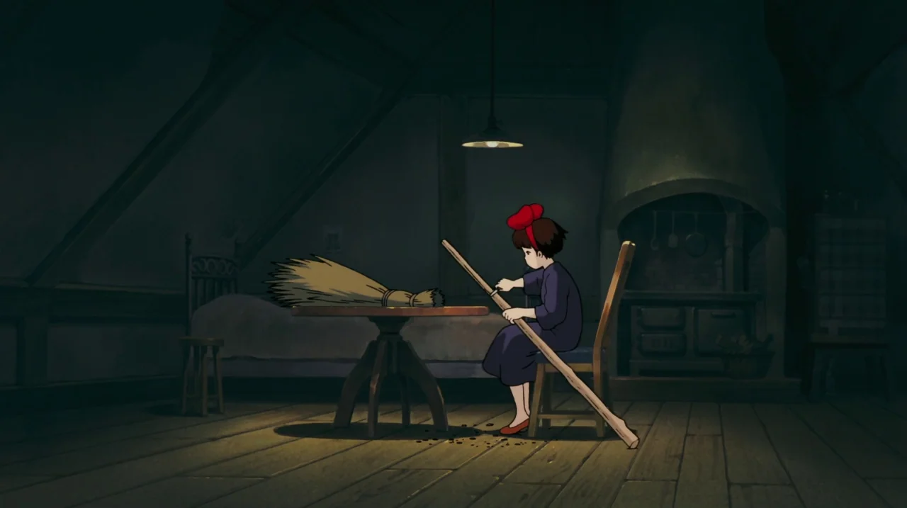 Kiki’s Delivery Service (1989) movie still: wide — A dimly lit wooden attic features a sloped ceiling and a large stone fireplace. A young girl sits…