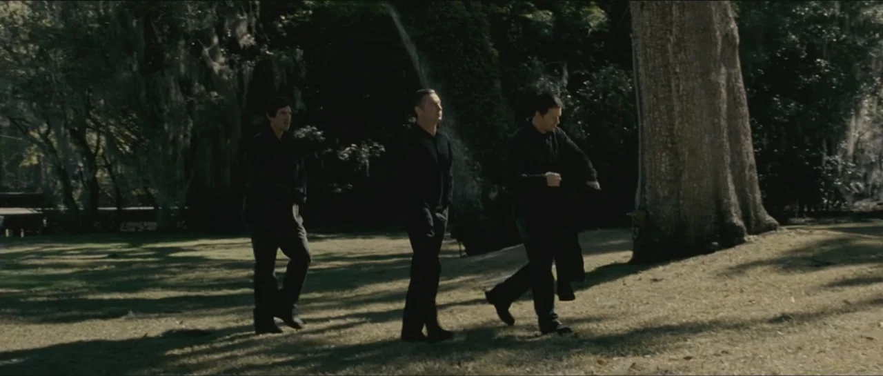 Contraband (2012) movie still: fullbody — A grassy clearing is surrounded by large trees draped with hanging Spanish moss. Three men walk in a line…