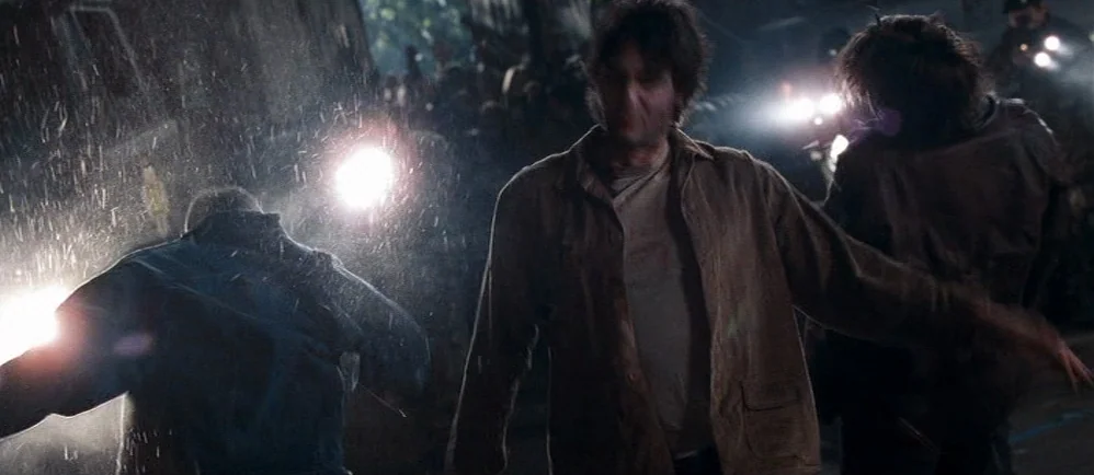 Shaun Of The Dead (2004) movie still: medium — A rain-slicked asphalt surface is illuminated by intense white light beams at night. People move…