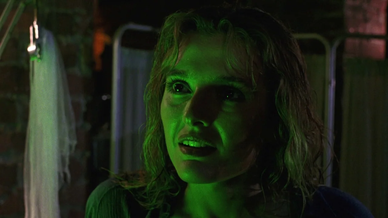 Bride of Reanimator (1989) movie still: closeup — A dimly lit room with medical privacy screens visible in the blurred background. A woman with damp…