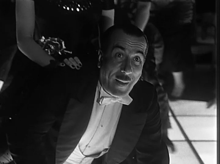 Variety Lights (1950) movie still: medium — A dark ballroom with a glossy light-colored floor featuring grid lines. A man in formal tuxedo attire…
