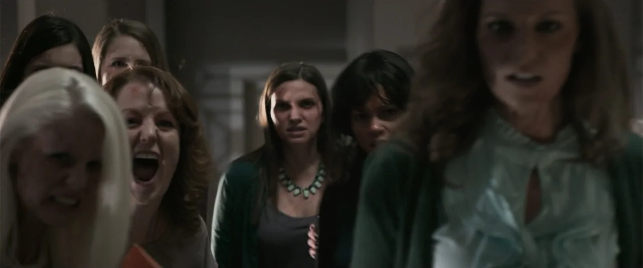 Office Uprising (2018) movie still: medium — A group of women are clustered together in a narrow, dimly lit indoor corridor. Several women in the…