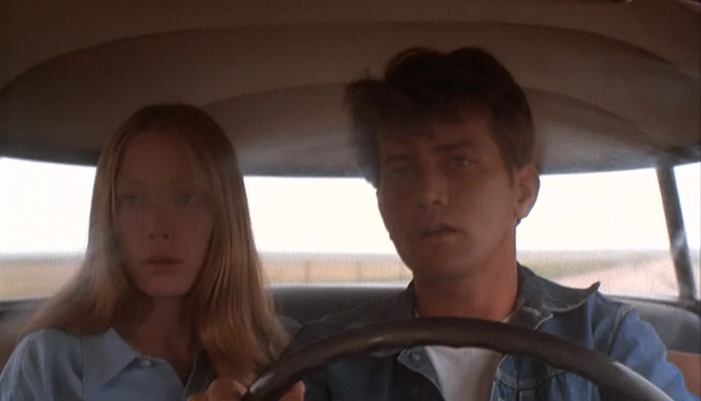 Badlands (1973) movie still: medium — The interior of a vintage automobile with light-colored upholstery and headliner. A young man and woman sit in…