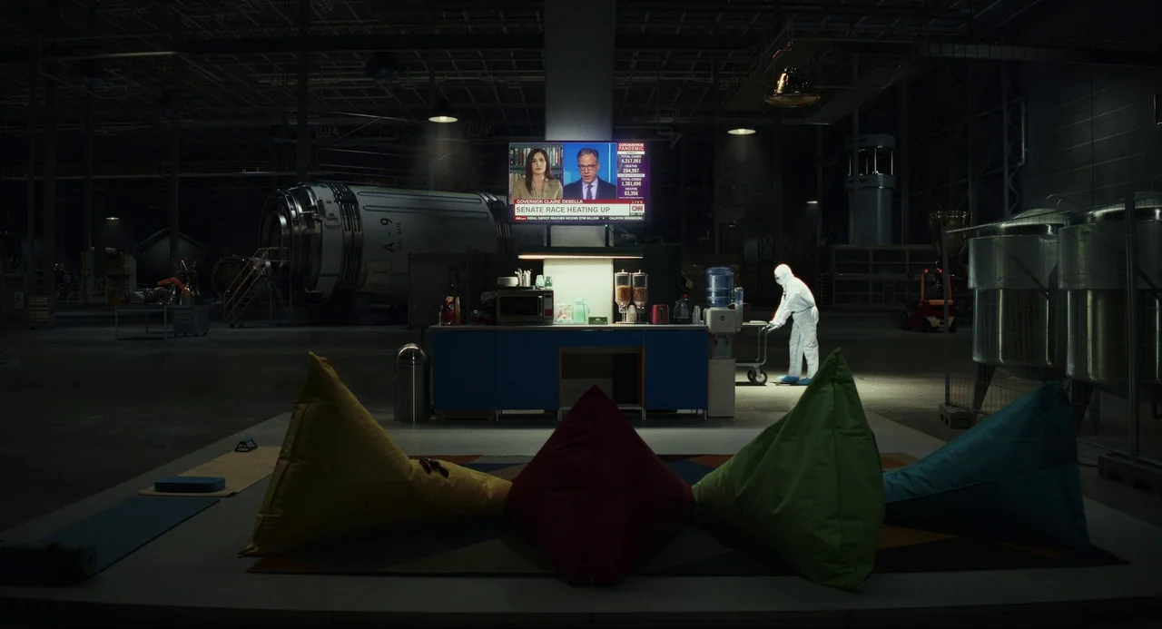 Glass Onion (2022) movie still: wide — A spacious industrial hangar contains a small makeshift break room with colorful beanbag chairs. A single…