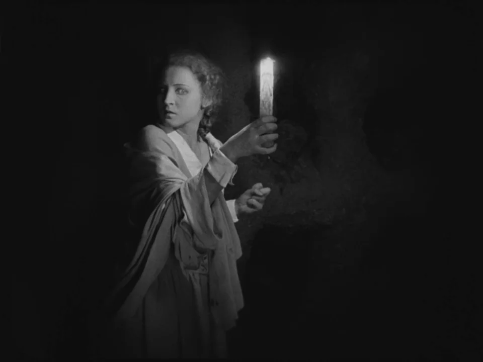 Metropolis (1927) movie still: medium — A dark, textured stone chamber surrounds a woman in an old-fashioned robe. She turns her head to look behind…
