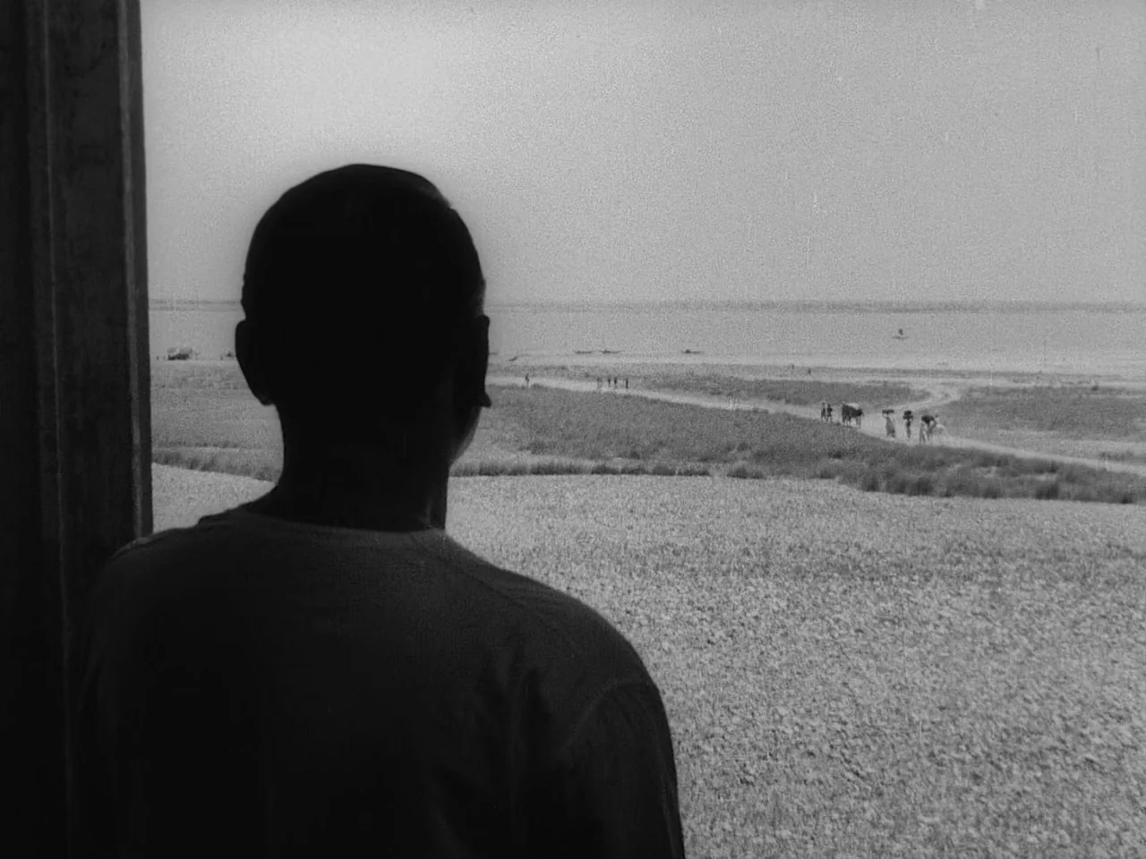 The Music Room (1958) movie still: medium — A man stands on a covered porch looking toward an open field and river. Small figures and livestock are…
