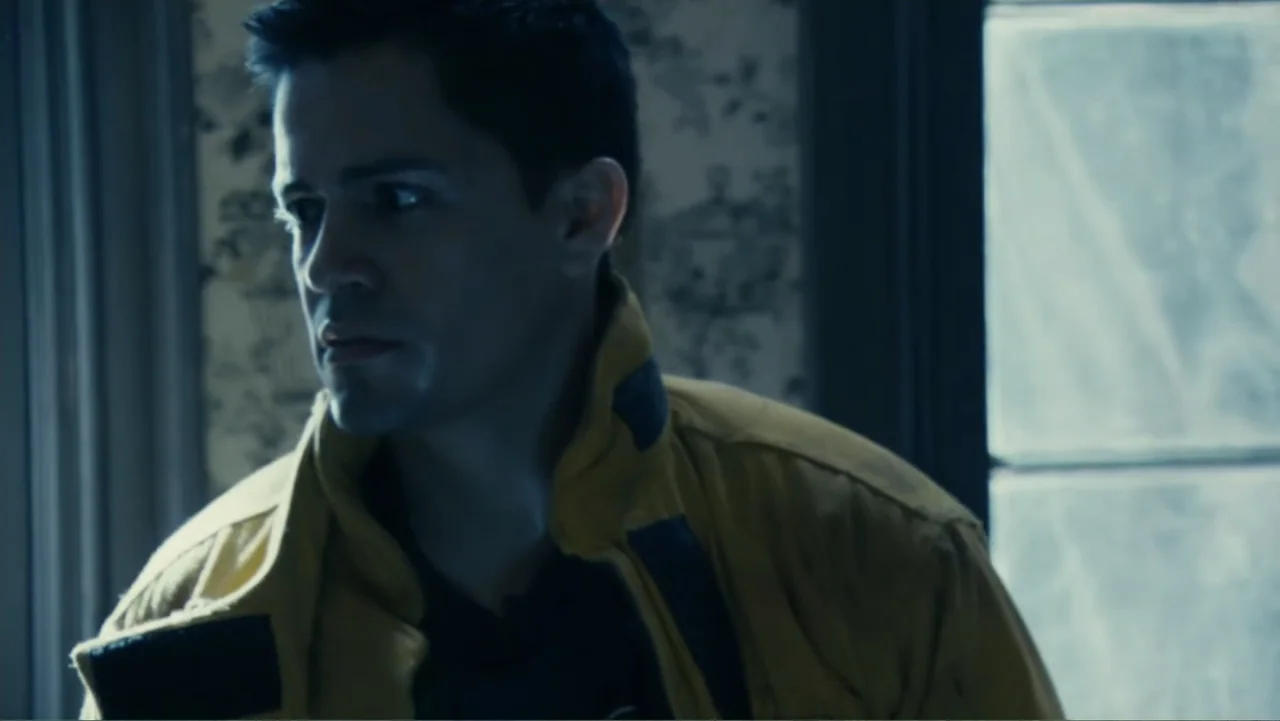 Quarantine (2008) movie still: medium — A man stands in an interior room with patterned wallpaper near a window. He looks toward the left side of…