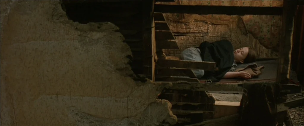 Down In The Valley (2005) movie still: wide — A ruined structure shows exposed wooden beams and crumbling wall plaster. A young woman lies resting…