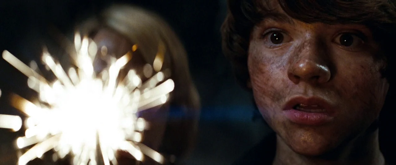 Super 8 (2011) movie still: closeup — A dark outdoor environment is illuminated primarily by the bright light of a handheld sparkler. A teenage boy…