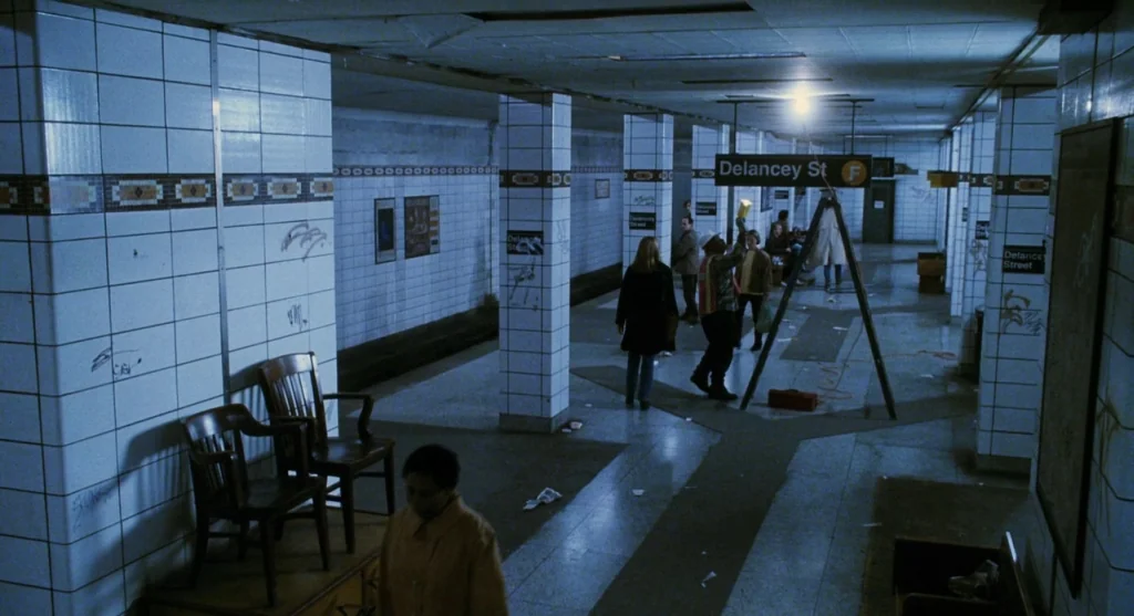 Mimic (1997) movie still: wide — A dimly lit New York subway station features cream-colored subway tiles with dark decorative trim. Several…