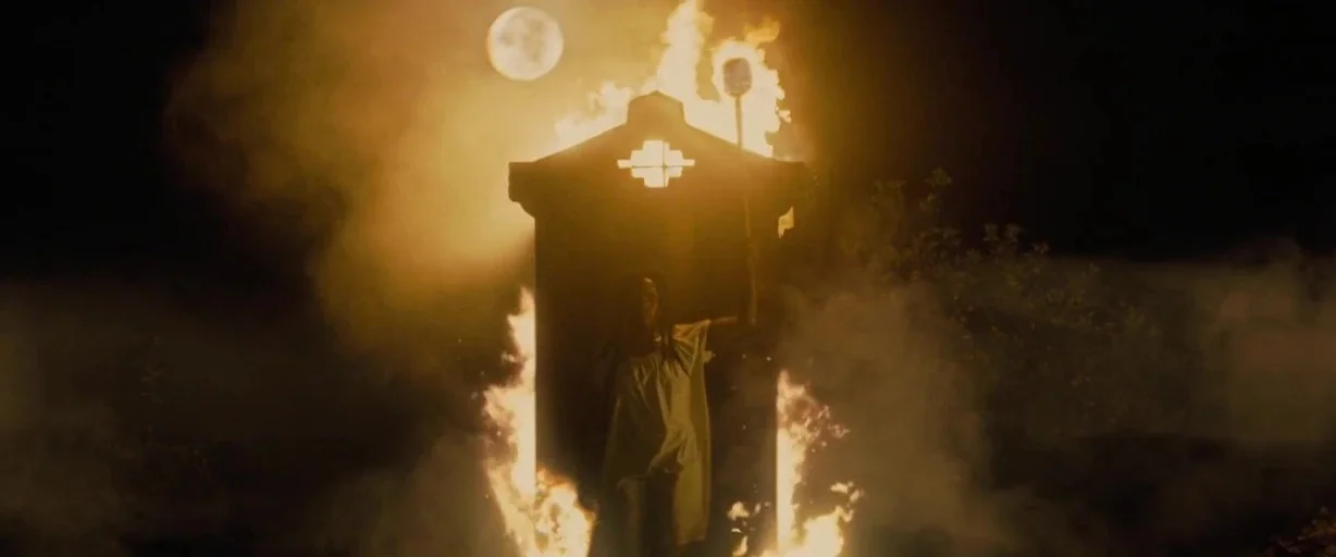 Antebellum (2020) movie still: wide — A dark, smoky outdoor space at night with a full moon visible above. A person in a white garment stands before…