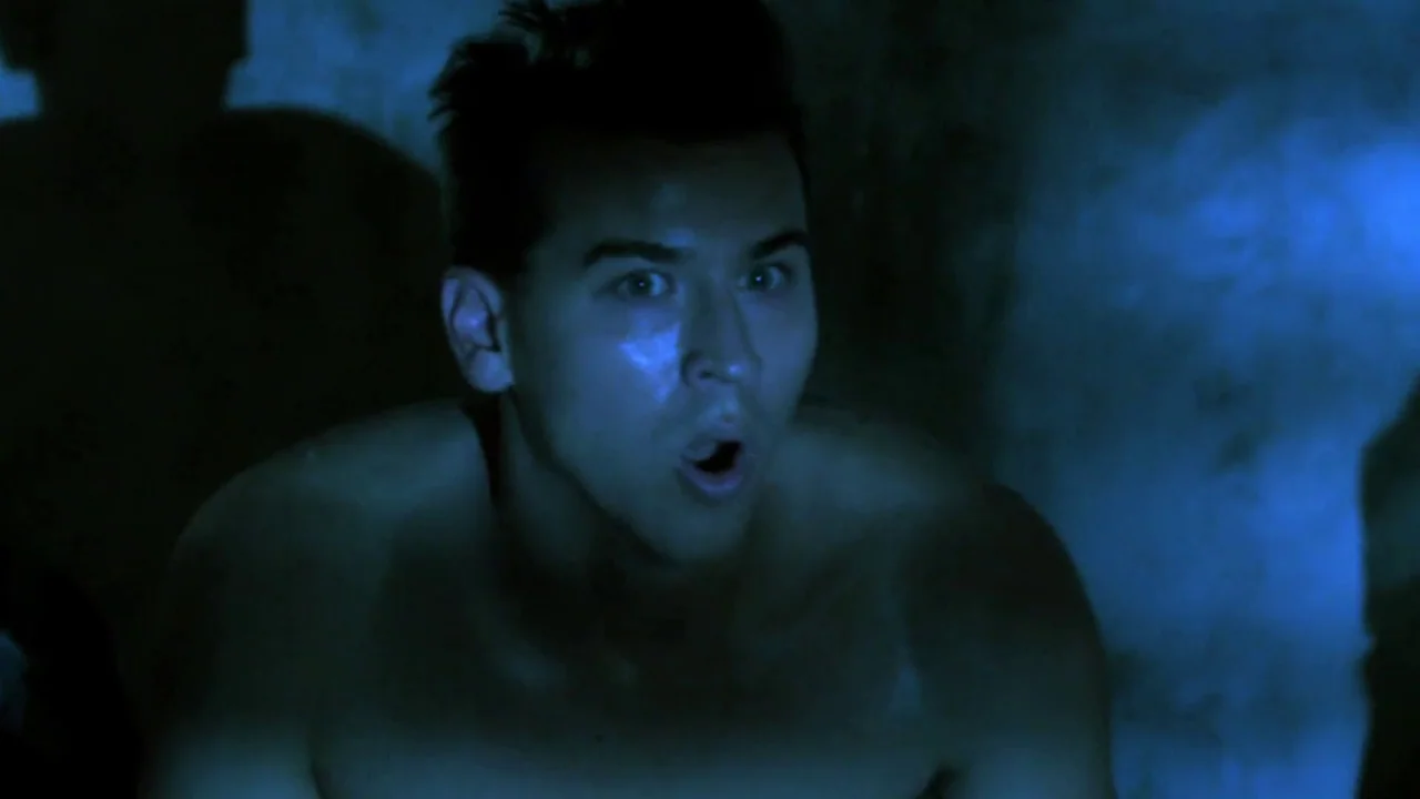 Hellraiser: Revelations movie still: closeup — A man stands in a dark environment with blue light casting shadows behind him. He stares forward with…
