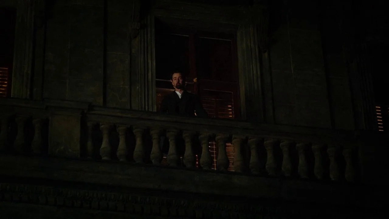 The Illusionist (2006) movie still: wide — A stone balcony of a dark building features an ornate balustrade against a night sky. A man stands…
