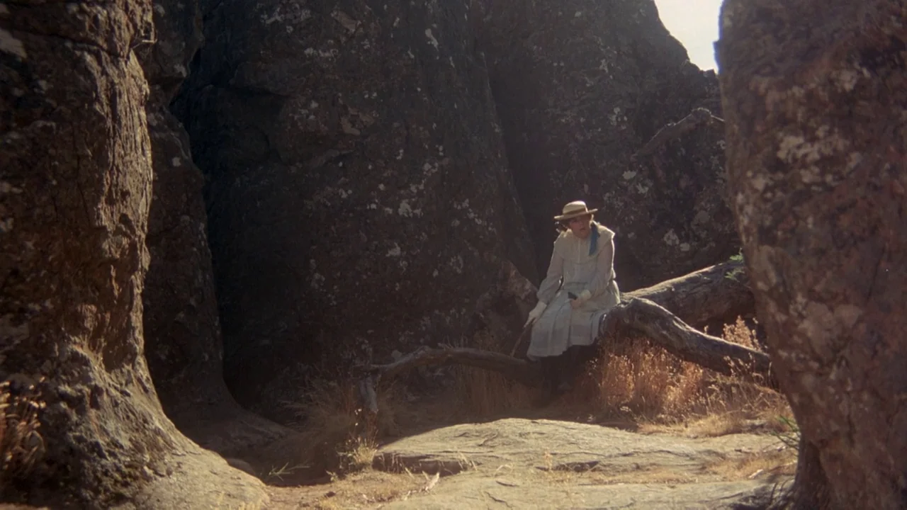Picnic at Hanging Rock (1975) movie still: wide — A desolate rocky outcrop features massive dark boulders and patches of dry dead grass. A lone…