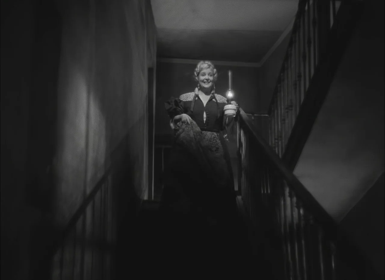 Les Enfants Du Paradis (1945) movie still: fullbody — A dark, narrow indoor staircase with a wooden banister leads down toward the camera. A smiling…