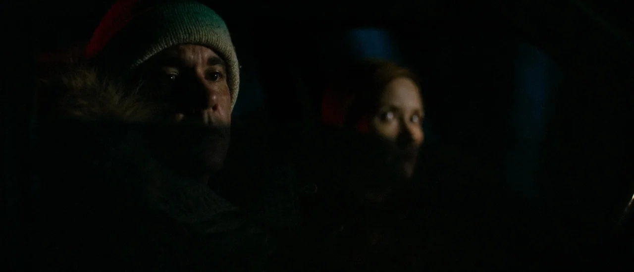 I Trapped The Devil (2019) movie still: medium — Inside a dark vehicle at night, two individuals sit in the front seats. A faint light source…