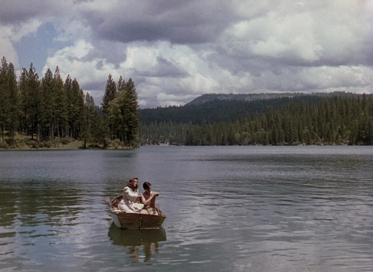 Leave Her To Heaven (1945) movie still: wide — A wooden boat floats on a vast lake surrounded by a dense evergreen forest. A woman and a young man…