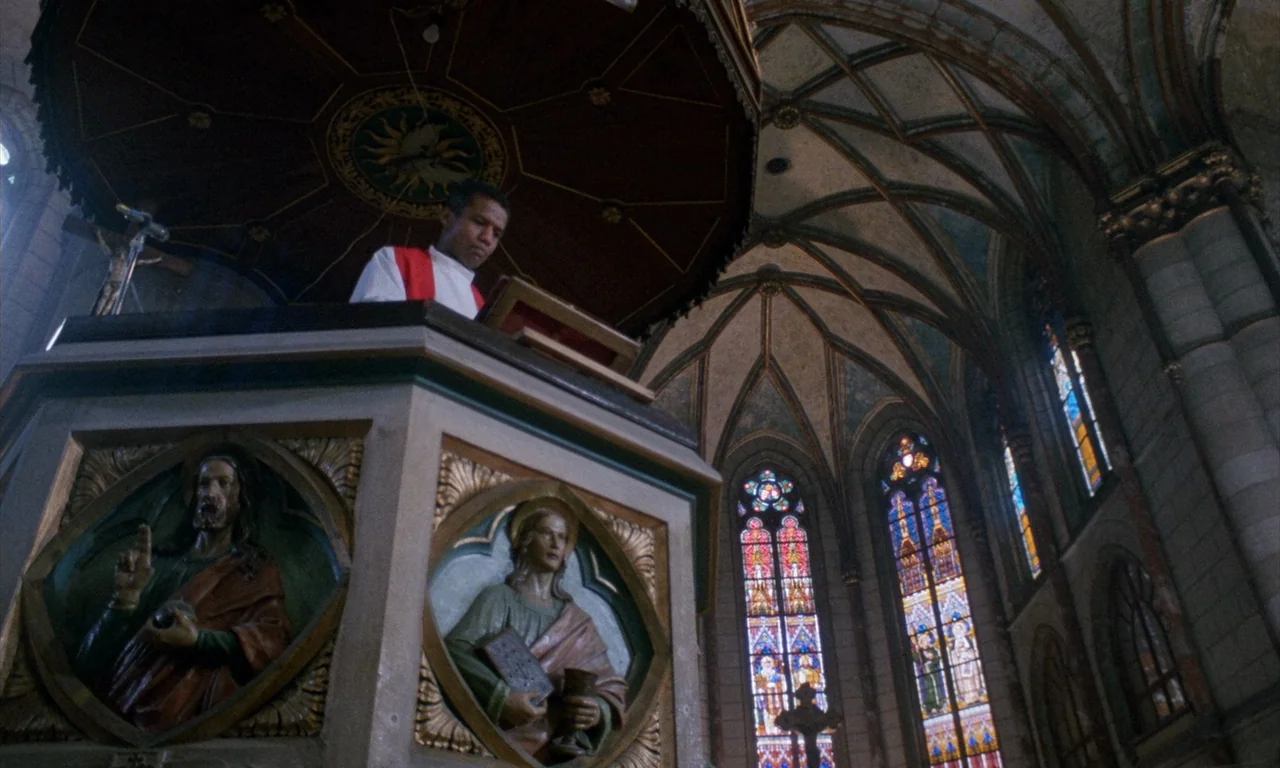 The Church (1989) movie still: medium — A stone cathedral interior with high arched ceilings and detailed religious carvings. A man in clerical…