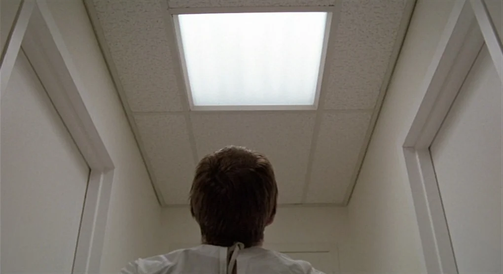 All That Jazz (1979) movie still: medium — A narrow hospital hallway with plain white walls and a recessed square ceiling light. A man wearing a…