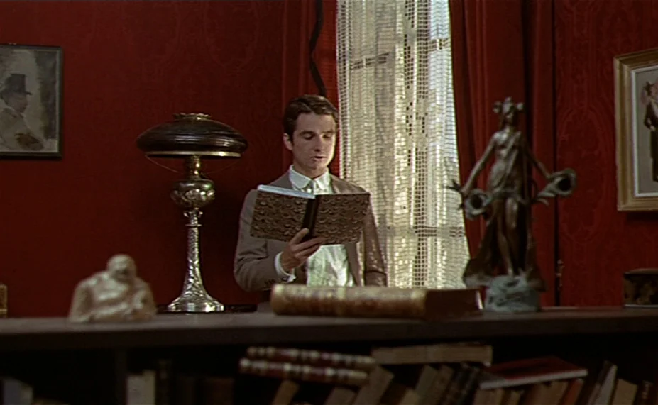 Two English Girls (1971) movie still: medium — A room with deep red wallpaper features a window with lace curtains. A young man stands in front of…