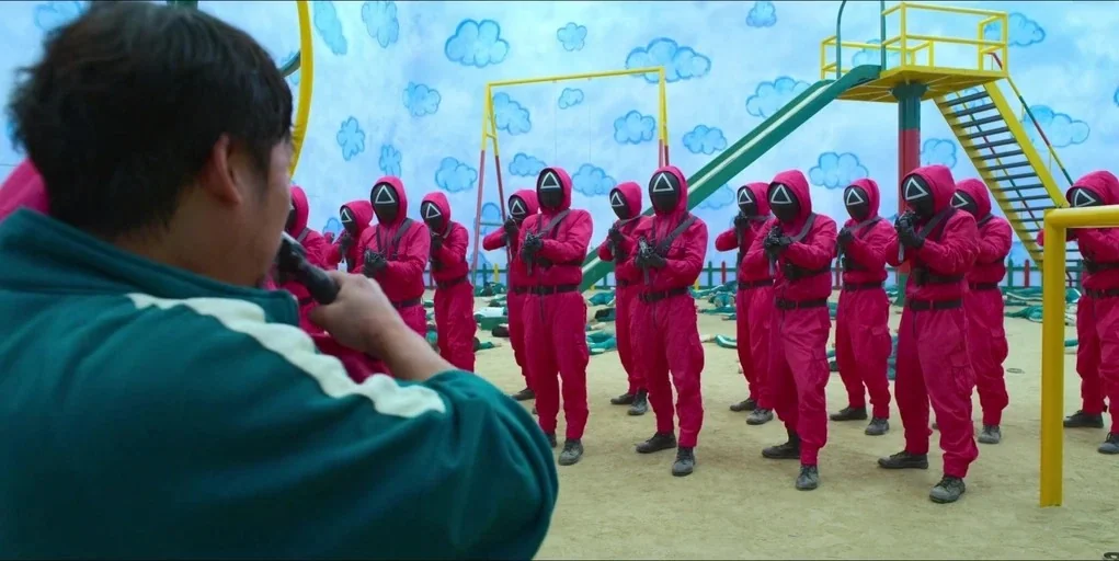 Making of: Squid Game (2021) movie still: medium — An indoor play area features painted walls with blue clouds and yellow equipment. A group of…