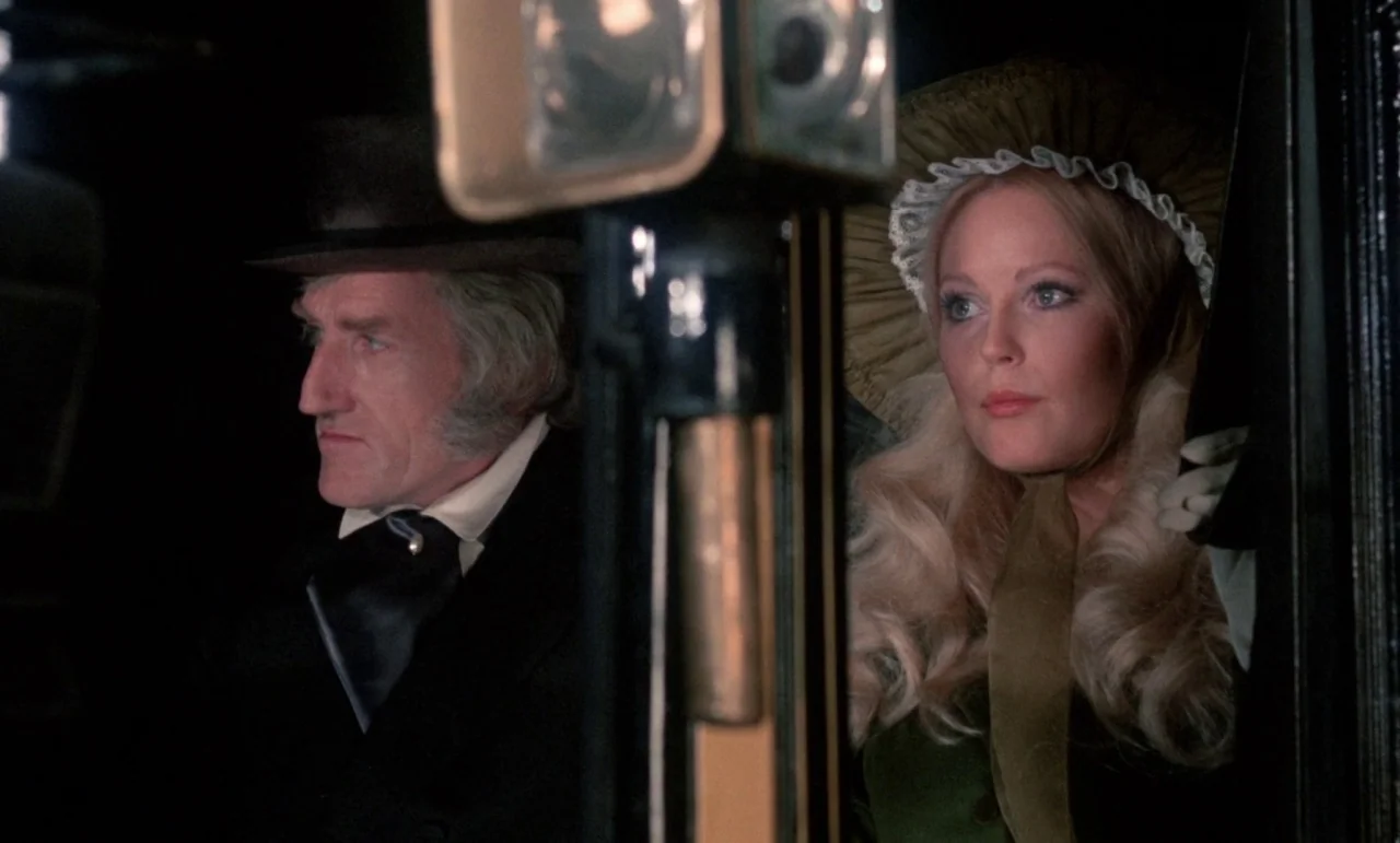The Horror of Frankenstein (1970) movie still: medium — A dark, cramped interior of a 19th-century horse-drawn carriage at night. An older man and a…