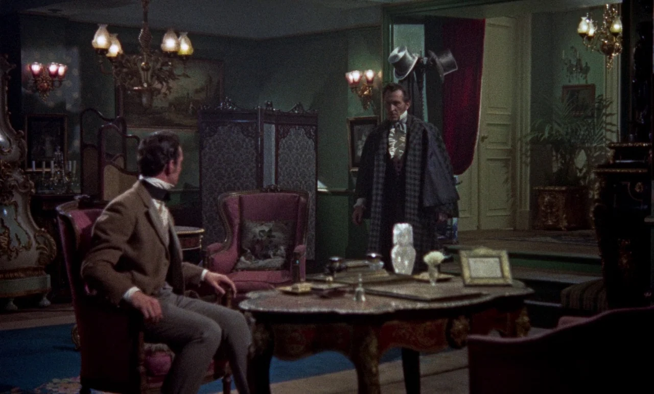 The Revenge of Frankenstein movie still: medium — A furnished parlor contains ornate vintage chairs, a central table, and decorative wall art. Two…