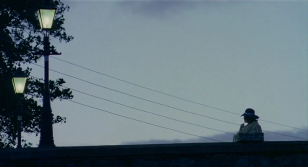 Breakfast On Pluto (2005) movie still: wide — A stone bridge sits under a twilight sky with electric lamps lining the path. A woman in a hat and…