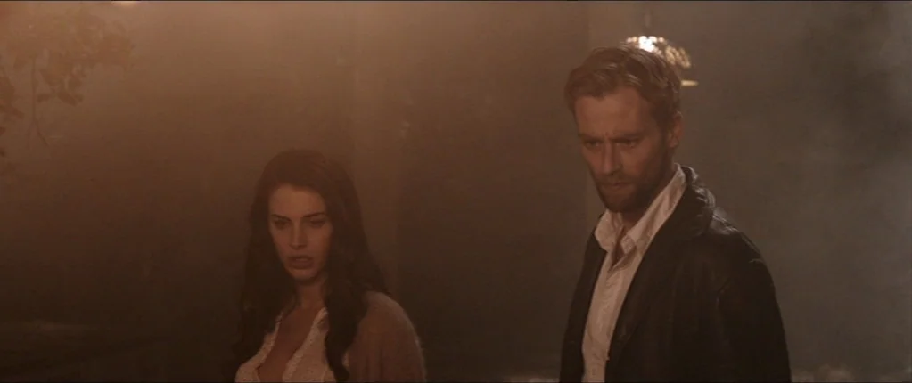 Abattoir (2016) movie still: medium — A dimly lit room is heavily filled with thick haze or smoke. A man and a woman stand close together while…