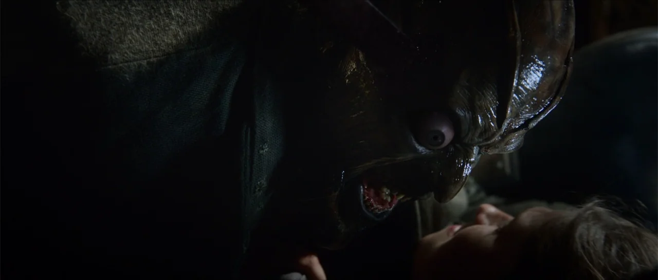 Jeepers Creepers 3 (2017) movie still: closeup — A dark and shadowy interior space features a tall, textured creature looming over a child. The…