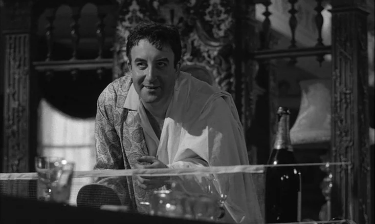 Lolita (1962) movie still: medium — A dimly lit room features ornate wooden furniture and an out-of-focus background. A man in a patterned robe…