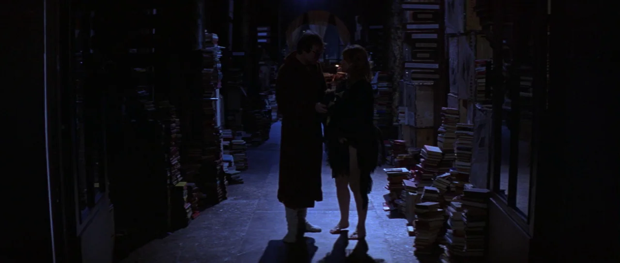 The Cook, The Thief, His Wife & Her Lover (1989) movie still: fullbody — A narrow aisle between towering stacks of books in a darkened room at…