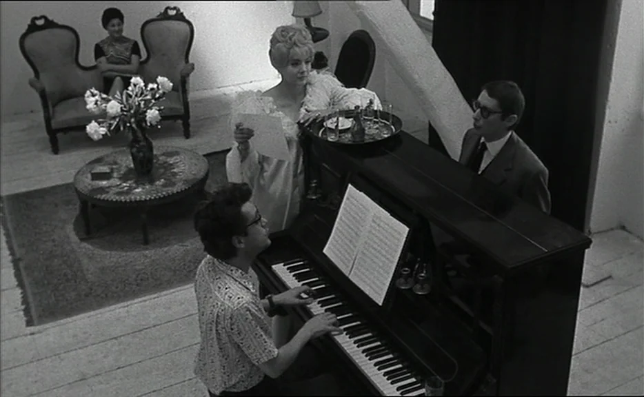 Cléo from 5 to 7 movie still: wide — A spacious room features white wooden flooring and antique furniture including a circular coffee table. A man…