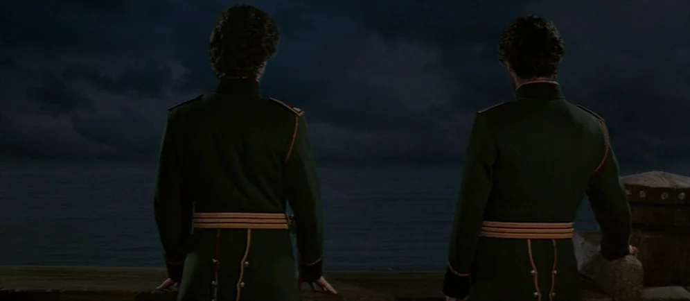 Dune (1984) movie still: medium — Two figures stand on a stone wall overlooking a dark, turbulent sea at night. The men wear matching 19th-century…