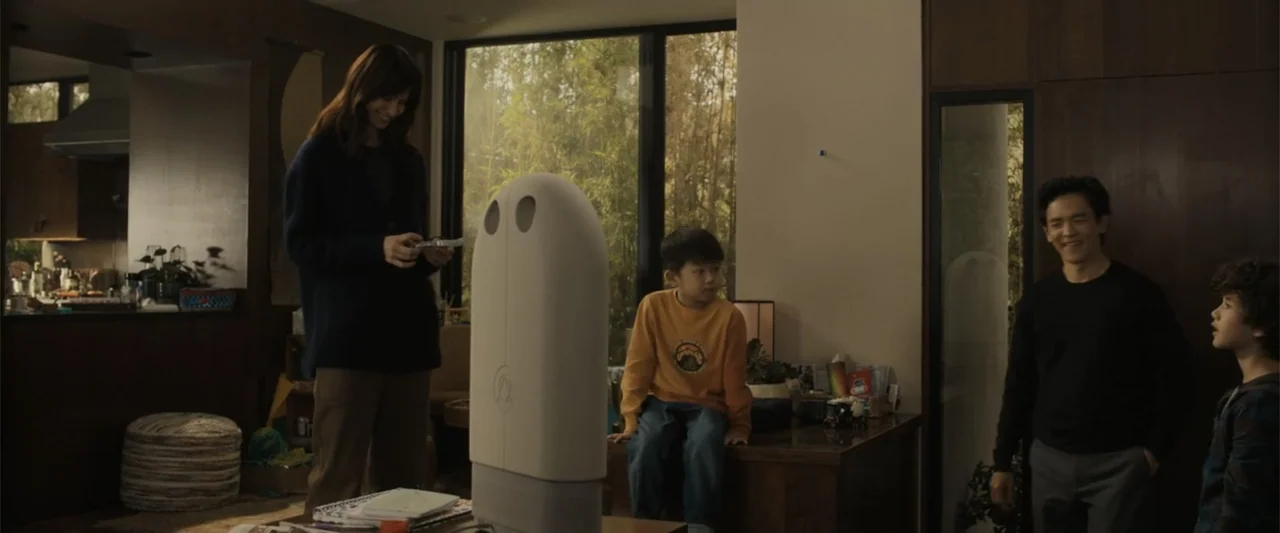 Afraid (2024) movie still: wide — A contemporary suburban interior with wood paneling and large floor-to-ceiling windows looking outdoors. A family…