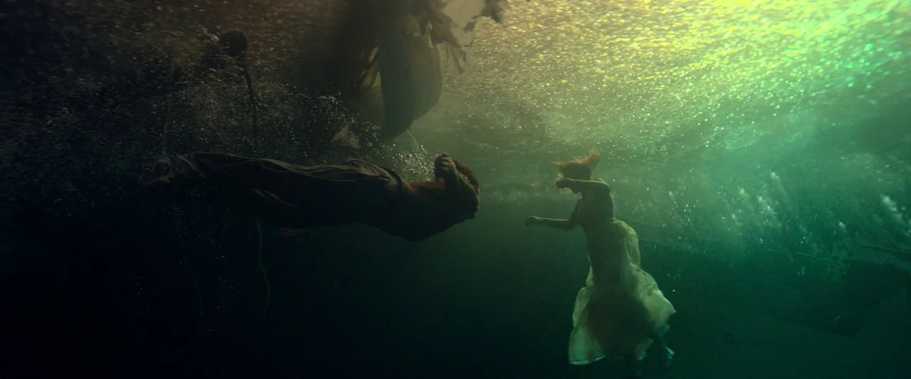 The Count of Monte-Cristo (2024) movie still: wide — Two people are submerged in deep, dark green water beneath a bright sunlit surface. The figures…